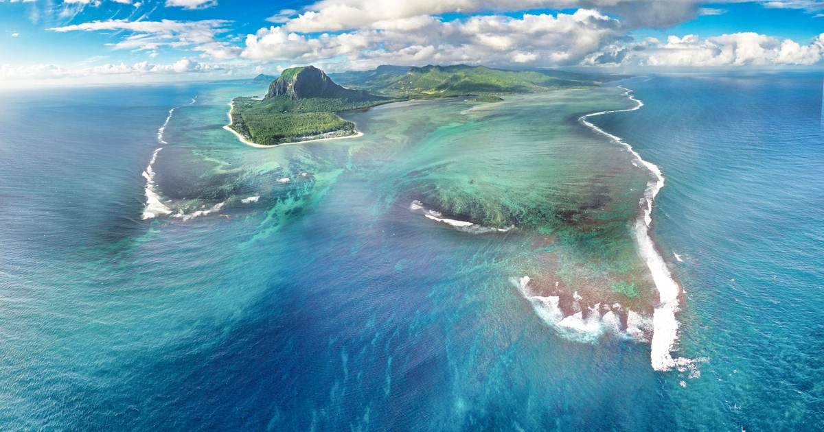 Вид с высоты на гору Ле-Морн и лагуну Маврикия с иллюзией подводного водопада, вокруг бирюзовая вода и облака
