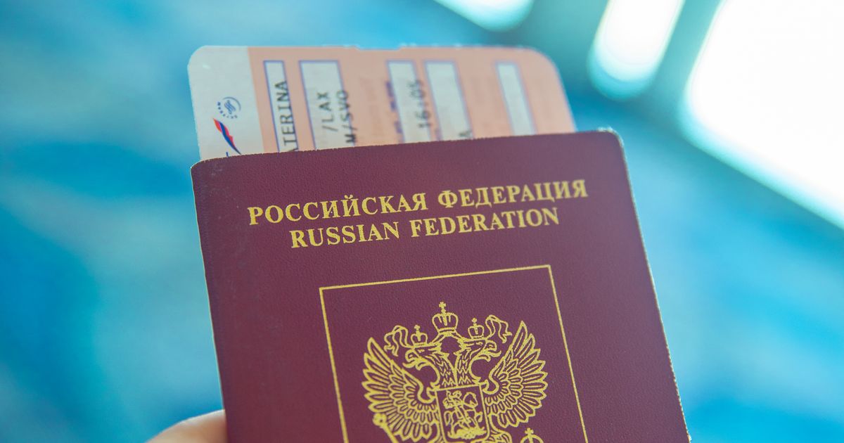 Рука держит крупным планом красный загранпаспорт гражданина Российской Федерации с вложенным посадочным талоном
